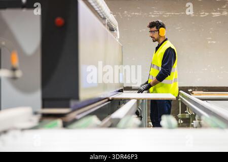 Worker operating industrial cutting machine in lumberyard Stock Photo