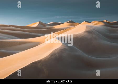 View of rippling sand dunes sculpted by wind under a serene sky create a mesmerizing landscape, casting long shadows and highlighting textures, Senek, Stock Photo