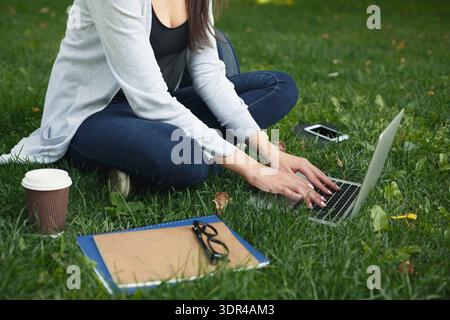 Writing on a Laptop in a Park While Enjoying Coffee and Taking Notes Stock Photo