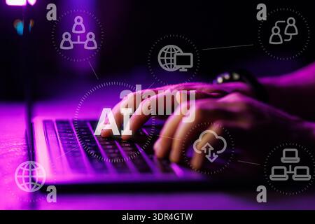 Close up of hands typing on a laptop keyboard with digital AI icons and overlays in a dark room with purple lighting, representing artificial intellig Stock Photo