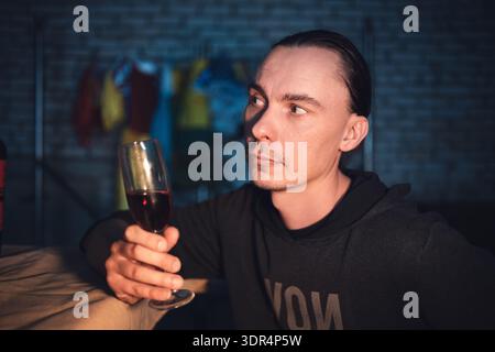 A man raises a glass of red wine and makes a toast, drinking against a dark background. Stock Photo