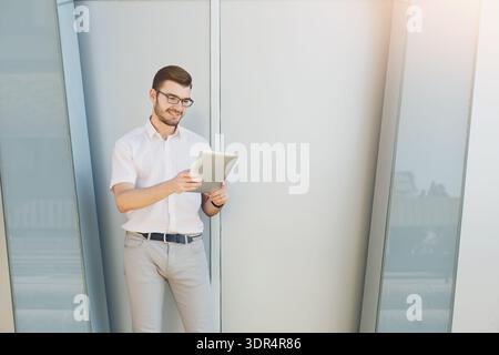 Young Man Smiles While Using Tablet in Modern Office Space During a Workday in the City Stock Photo