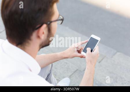 Man Using Smartphone While Sitting on Steps in an Outdoor Setting Stock Photo
