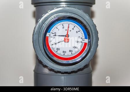 Close-up of circular temperature and pressure gauge mounted on a gray plastic pipe system. Stock Photo