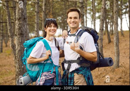 Happy couple of hikers with backpacks smiling in forest, standing together in team Stock Photo