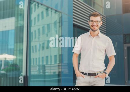 Man Stands Confidently in Front of Modern Building During Sunny Day Smiling at Camera Stock Photo