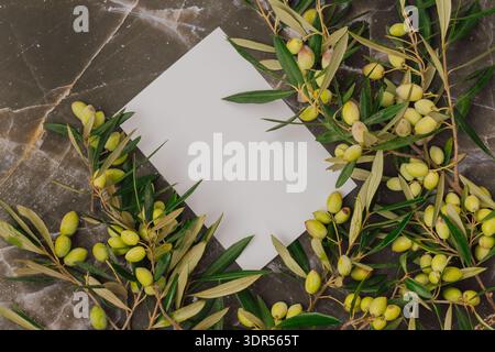 Premium olive oil branding mockup with fresh green olives on marble. Blank white card for logo text Stock Photo