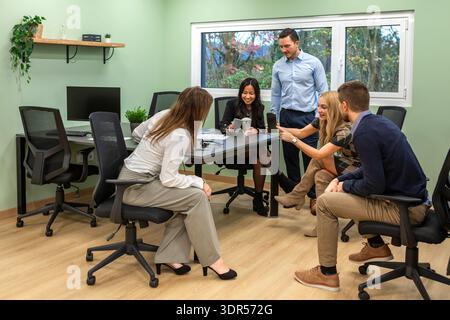 Diverse business group smiling together while viewing phone screen during break in coworking office Stock Photo