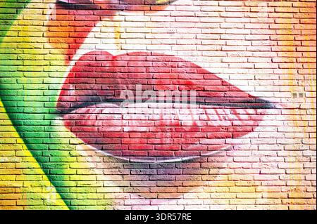 Vibrant urban graffiti art featuring a large pair of red lips painted onto a textured brick wall, adding a pop of color to the city environment. Stock Photo