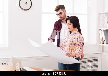 Couple Discussing Project Details While Looking at Large Paper in Bright Room Stock Photo