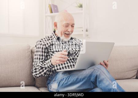 Senior Man Using Laptop and Smiling While Sitting on a Couch at Home Stock Photo