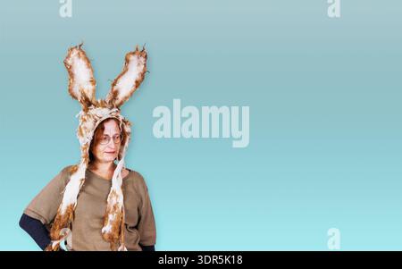 Sstudio portrait of a middle aged woman wearing handmade felted bunny hat with long ears standing against blue background. Copy space Stock Photo