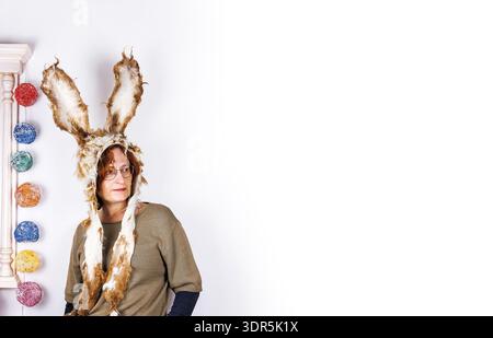 Sstudio portrait of a middle aged woman wearing handmade felted bunny hat with long ears standing against white background. Copy space Stock Photo