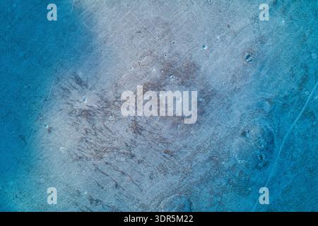 Frosty earth surface reveals intricate abstract patterns of snow and withered grass in this cold minimalist winter texture capturing the silent beauty of frozen soil from a high drone view. Stock Photo