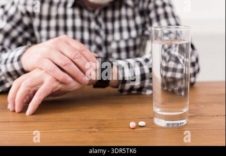 Senior Man Checks Watch While Preparing to Take Medication With Water on Wooden Table Stock Photo