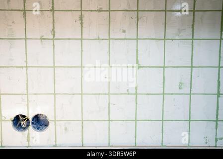 Tiling backsplash wall in a kitchen, applying light green grout to ceramic tile joints, undertaking home renovation, improvement, and construction project Stock Photo