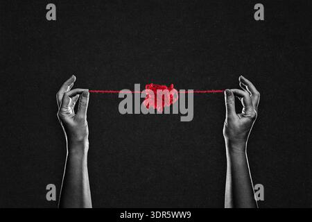 Two Hands Pulling Red String from Tangled Yarn Ball in Black and White on Textured Paper Background Stock Photo
