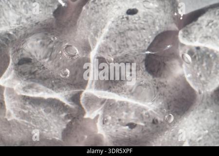 Transparent liquid gel showing abstract water ripples and light reflections on grey background Stock Photo