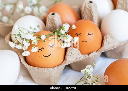Cute easter eggs with funny faces in brown box with flowers background. Easter holiday concept with cute handmade eggs in floral wreath crowns. Stock Photo