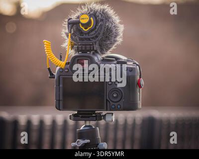 Mirrorless camera with external DEITY microphone mounted on tripod outdoors in warm evening light Stock Photo