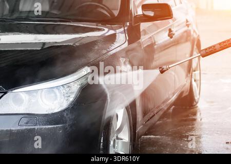A man washes his car at a self service car wash. The car is washed using high pressure water. Self-service car wash. Stock Photo