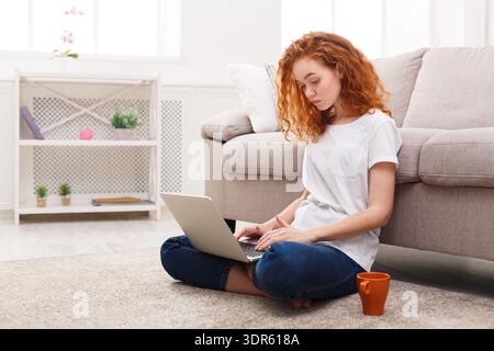 Young Woman Works on Laptop While Sitting on Floor With Coffee in Bright Living Room Stock Photo