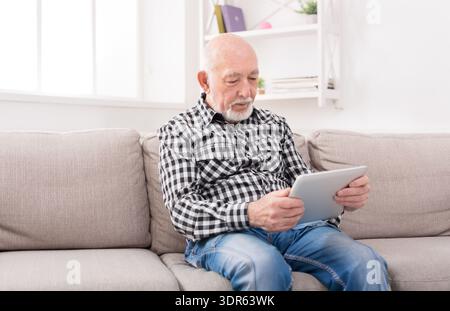 Senior Man Using a Tablet While Sitting on a Couch in a Cozy Living Room Stock Photo