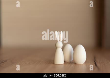 Minimal easter still life with white bunny and eggs. Minimal still life of small white wooden bunny figurine and two eggs on rustic table with soft Stock Photo