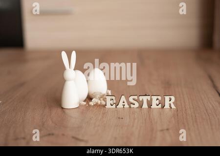 Minimal easter decor with bunny and eggs on wooden floor. Minimal Easter still life on wooden floor with white bunny figurine, eggs and wooden letter Stock Photo