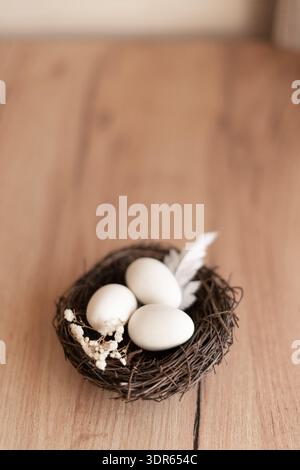 Bird Nest with Three White Eggs on Rustic Wooden Background. Small birds nest with three white eggs, feather dried flowers on a rustic wooden surface Stock Photo