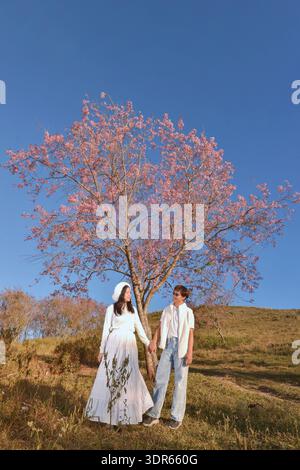 Happy young couple standing in the countryside holding hands, Thailand Stock Photo