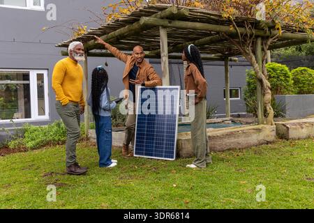 African American family standing in yard by pergola pointing to solar panel while child using phone Stock Photo