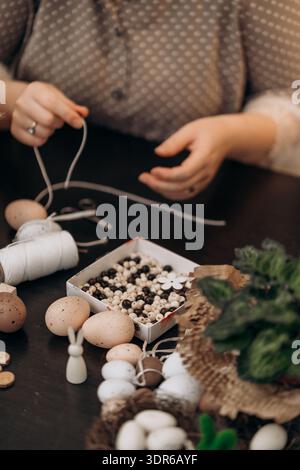 Hands crafting handmade easter decorations with wooden eggs. Woman crafting Easter decorations, threading string and arranging wooden eggs and beads Stock Photo