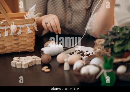 Hands crafting Easter decorations with eggs and beads at home. Close up of hands crafting Easter decorations on a table with eggs, beads, twine Stock Photo