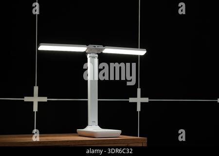 A sleek, contemporary desk lamp featuring dual illuminated bars and flexible positioning, set against a dark background with minimalist white grid lin Stock Photo