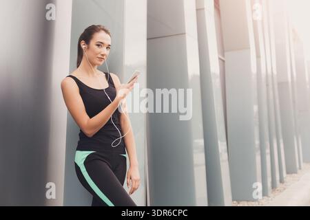 Young Woman Enjoying Music While Leaning Against Modern Building in Urban Setting Stock Photo
