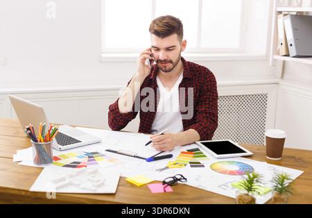 Man Working in an Office Space During the Day While Talking on the Phone and Drawing Stock Photo