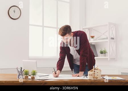 Man Working on Architectural Plans in Modern Office With Plants and Model House Stock Photo