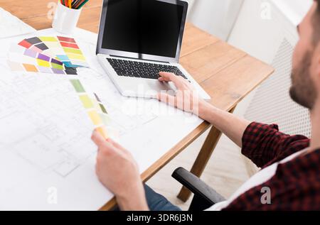 Designer Works at Desk Using Laptop and Color Palette in Bright Workspace Stock Photo