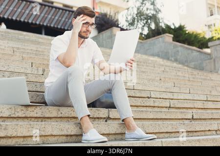 Man Reading Document While Sitting on Steps in Urban Area During Daylight Hours Stock Photo