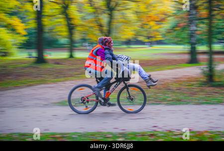 Couple riding a bicycle together through autumn foliage in Tiergarten park, Berlin, Germany Stock Photo