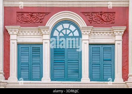 Colorful turquoise shuttered windows on a historic shophouse facade in Chinatown, Singapore, showcasing ornate colonial architecture. Stock Photo