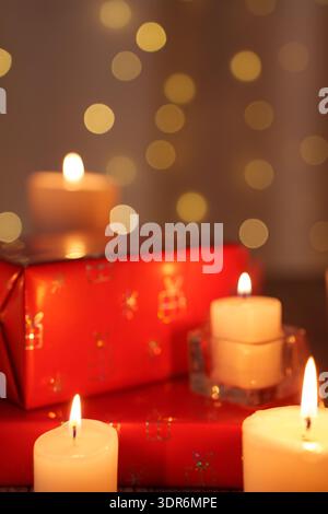 warm candlelit christmas ambience featuring bright red wrapped gift and soft bokeh lights in a cozy festive setting with glowing candle flames and hol Stock Photo