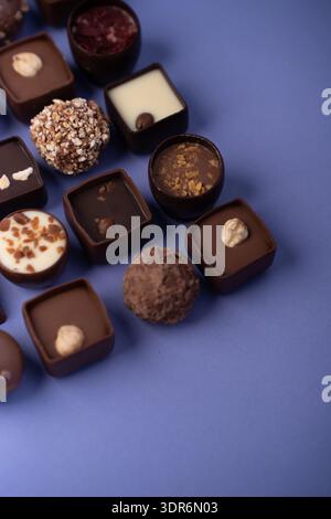 close-up assortment of gourmet chocolate pralines and truffles arranged on a matte lavender-blue background, highlighting glossy ganache, nut toppings Stock Photo