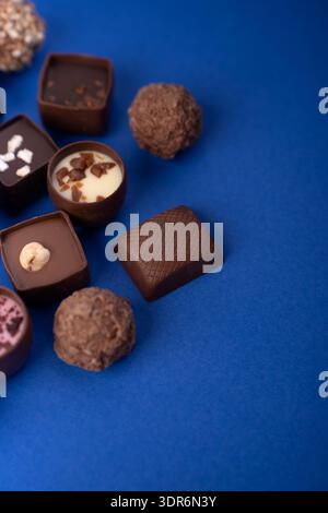 close-up assortment of artisanal gourmet chocolates and truffles arranged on a vivid cobalt-blue backdrop, showcasing textured pralines, glossy shells Stock Photo