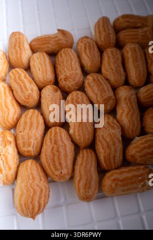 close-up overhead view of neatly arranged golden-brown piped choux pastries (mini eclairs) on a white grid tray, showcasing textured ridges, warm high Stock Photo