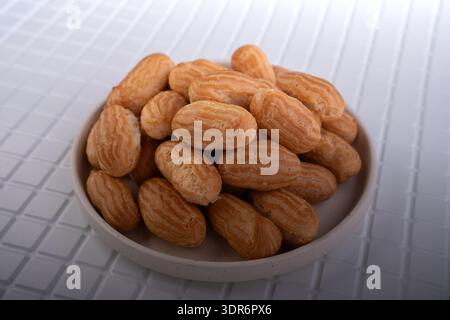 close-up of a pile of small golden choux pastries (mini éclairs) stacked on a white ceramic plate atop a glossy white tiled surface, warm studio light Stock Photo