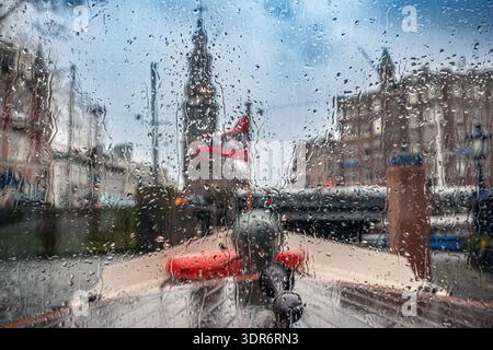 View from a moving boat in the canals of Amsterdam, Netherlands, with raindrops on the window screen and blurred houses beyond. Stock Photo