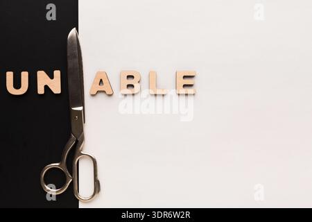 Scissors Placed Next to Wooden Letters Spelling Unable on Black and White Background Stock Photo