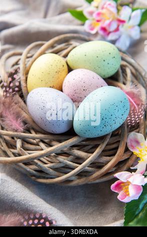 Pastel colored speckled easter eggs resting in a wicker nest with spring flowers and feathers Stock Photo